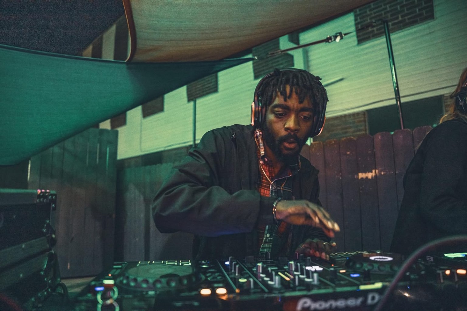 DJMALCOLMXTC in a black jacket and headphones, mixing at his controller